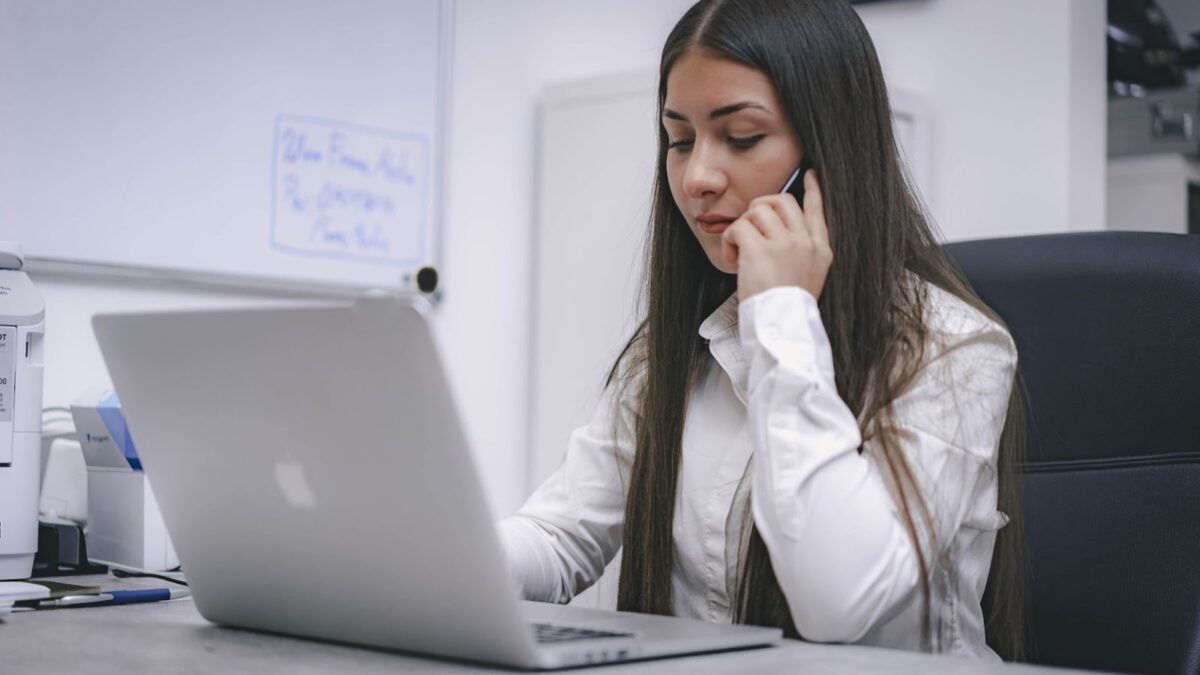 Real estate agent in front of laptop, making a phone call on smartphone