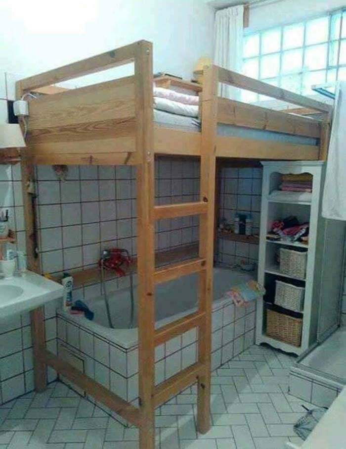 A tiled bathroom with a wooden bunk bed built over the soaking tub, complete with a ladder to reach the bed.