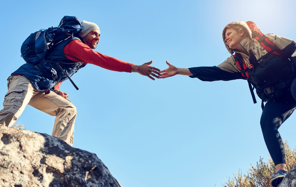 Person assisting another person over rocky terrain on a hike.