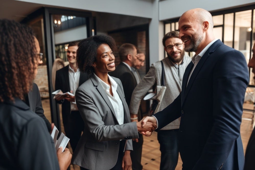 People in a room for a networking event, dressed professionally in suits and shaking hands.