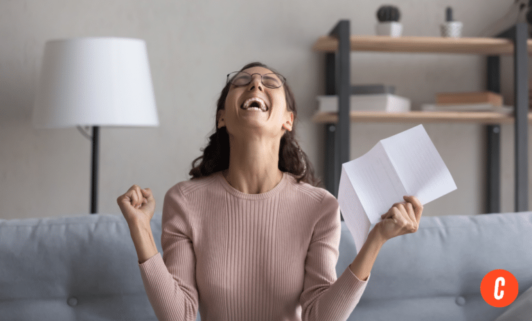 Latina woman sitting on couch at home excited by good news, celebrating with a letter in her hands.