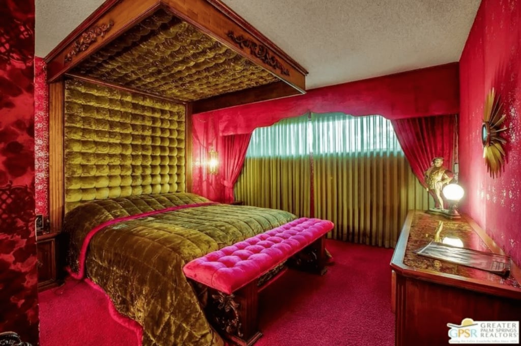 A bedroom with a bed covered in green duvet, fuchsia bench, fuchsia carpet, and fuchsia curtains