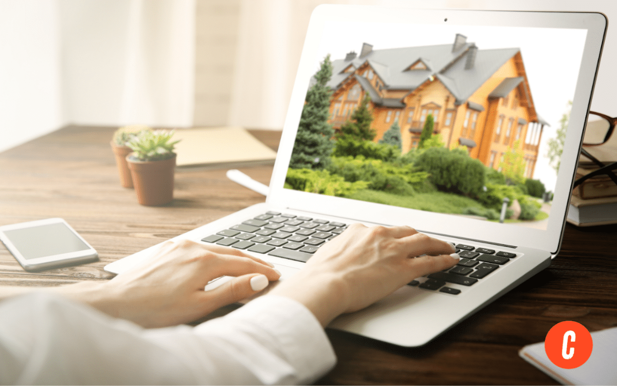 Woman typing on a computer, looking on a website with a large wooden house.