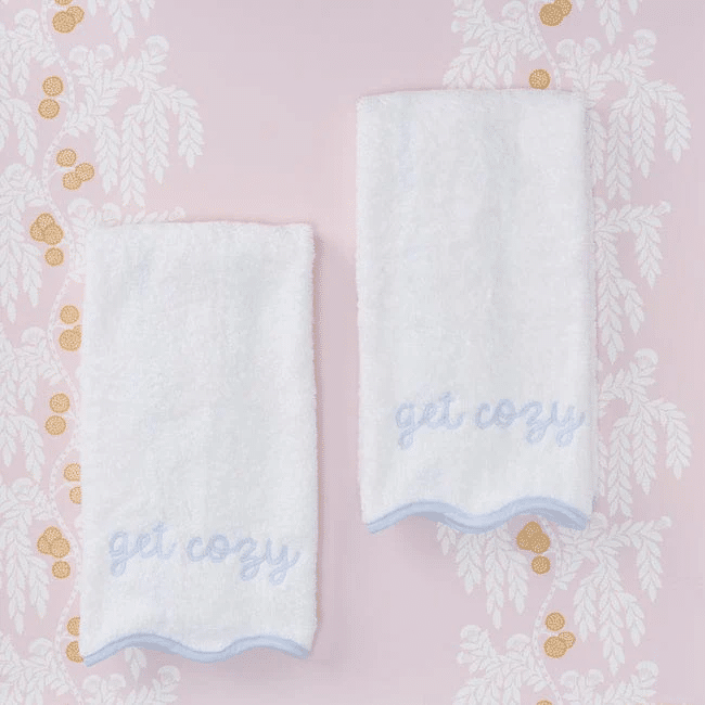 White hand towels with blue embroidery over a pink wall paper background