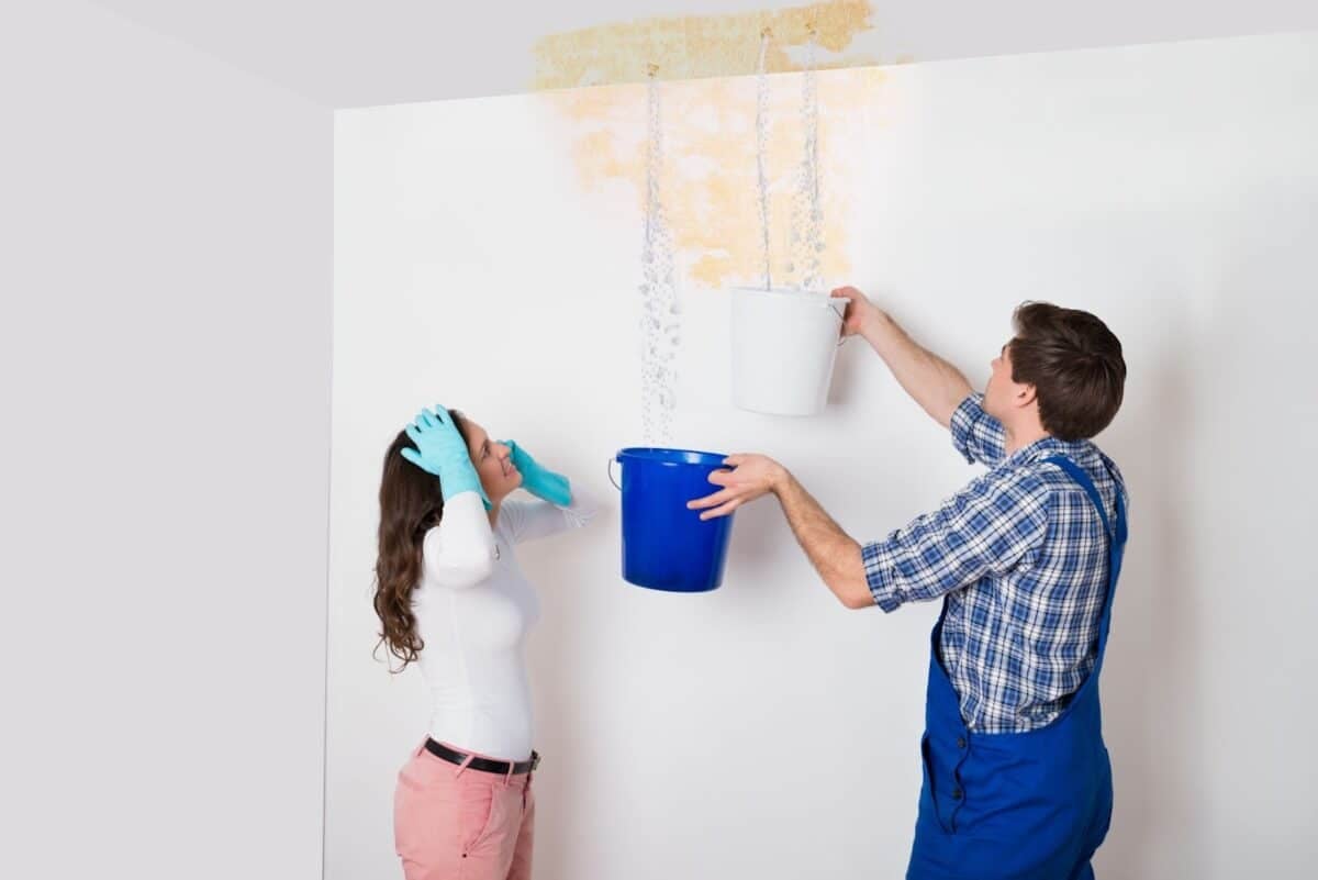 Man and woman collecting water in a bucket from a leak in the ceiling. 