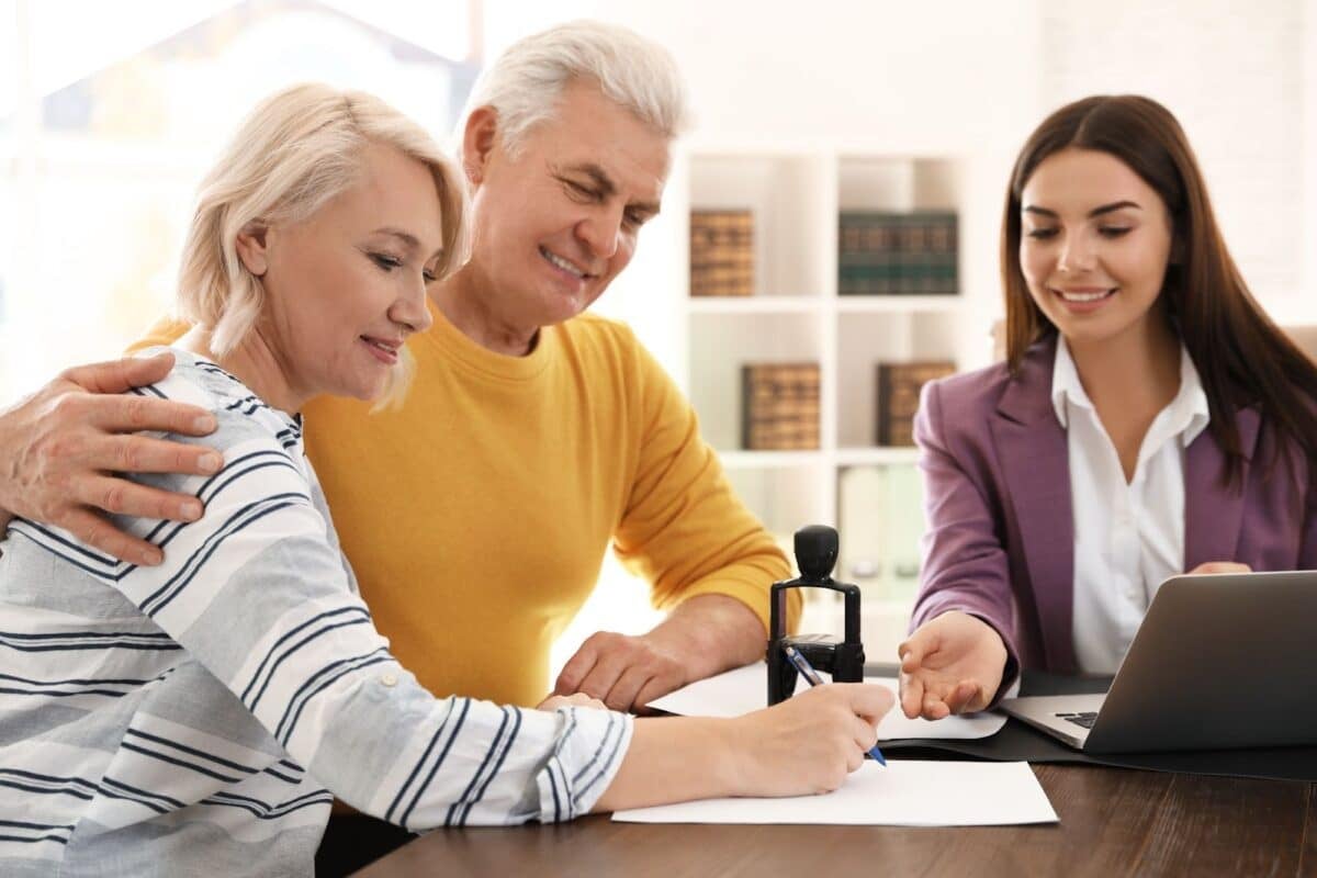 A real estate agent meeting with a couple who is signing a piece of paper.