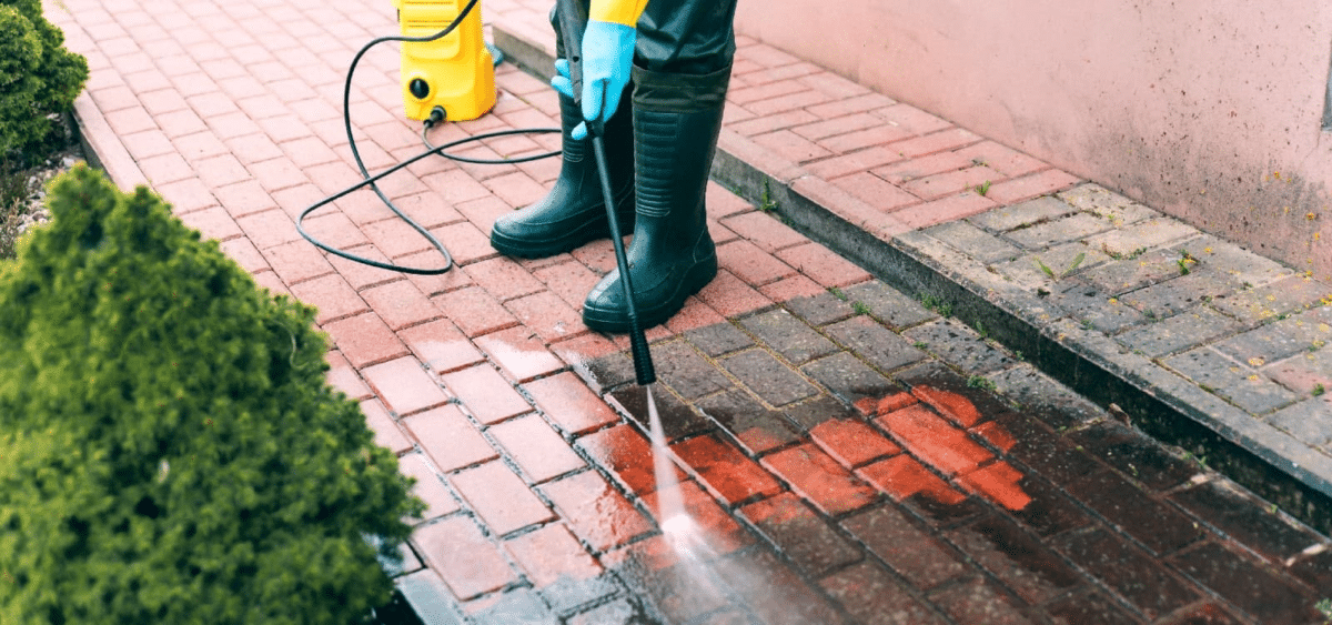 Person wearing boots and gloves power-washing a walkway