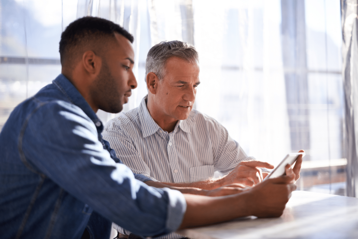 Two real estate agents sitting at a table and looking at a tablet.