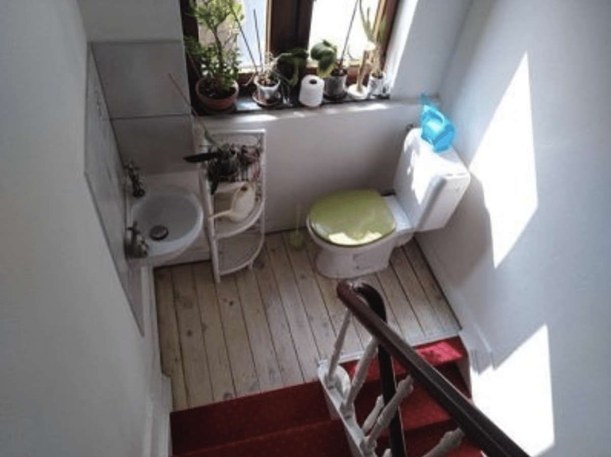 Toilet, sink, and small shelf near a window on the landing of a set of stairs.