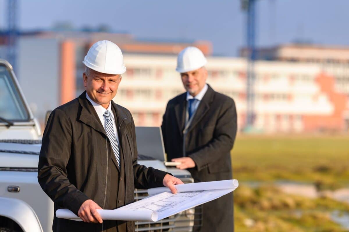 Two architects at construction site review plans.