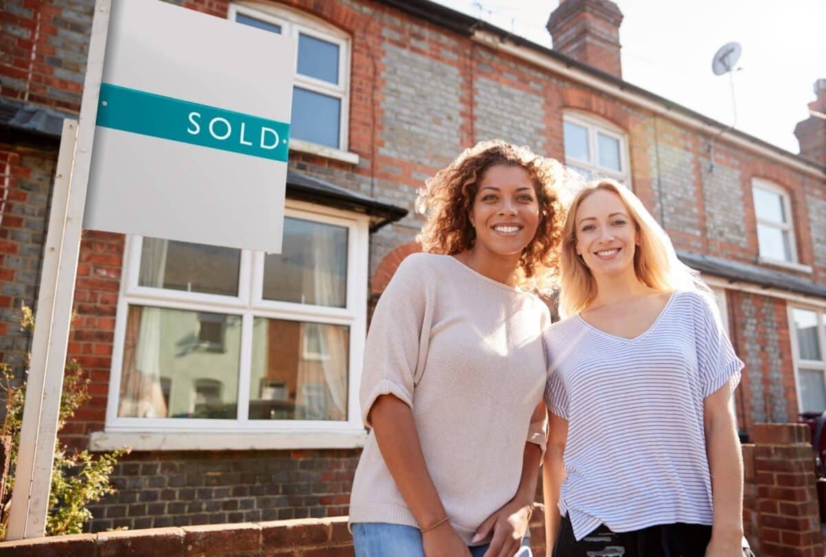 Portrait of two women standing outside a new home with a sold sign.