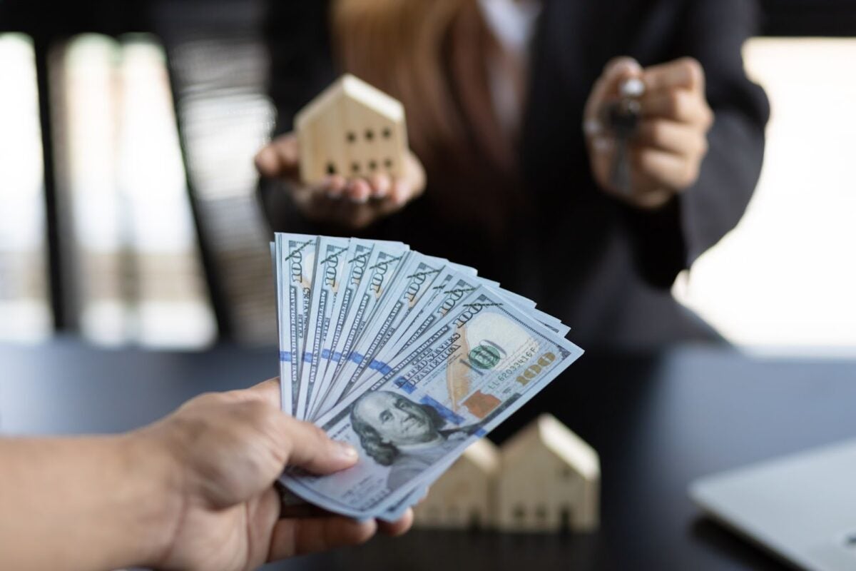 Hand holding money trading with another hand holding a key and toy house.