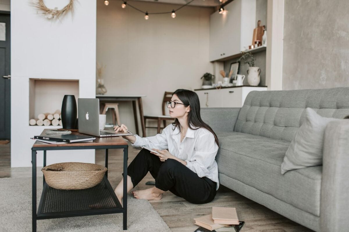 Woman sitting in front of a couch working on her laptop.