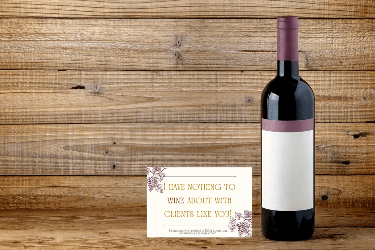 A bottle of red wine next to a sample wine label with a thank you note written on it.