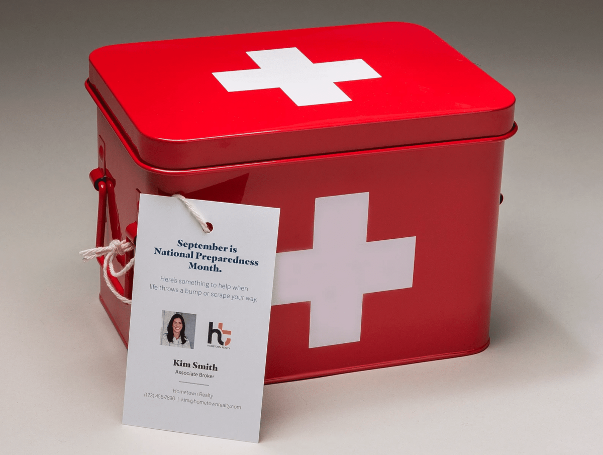 A first aid kit with a national preparedness month card leaning on it along with real estate agent contact information.