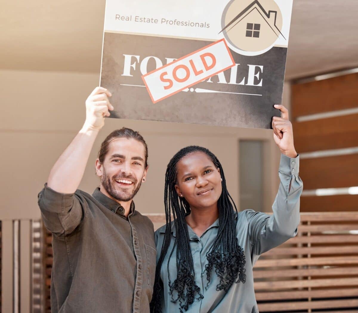 Shot of a young couple holding up a sold board outside their house.