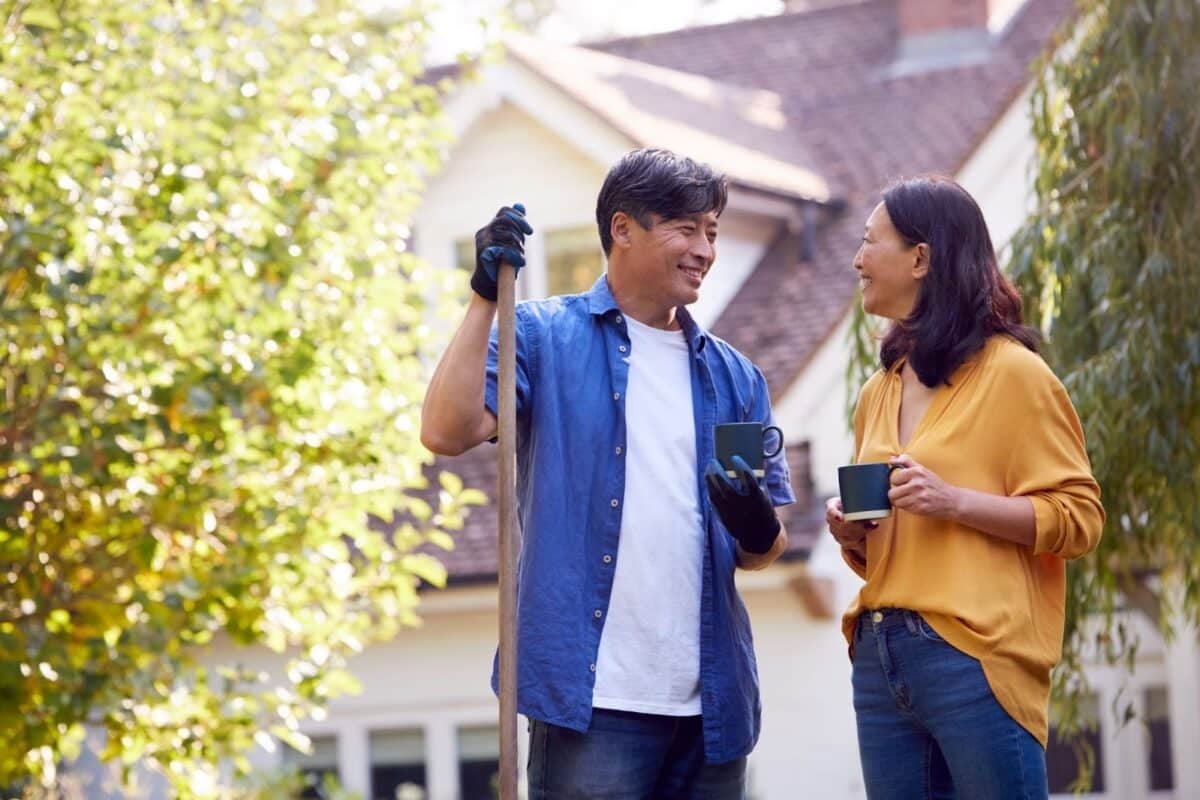 Mature couple taking a break with hot drinks while tidying the garden with rake.