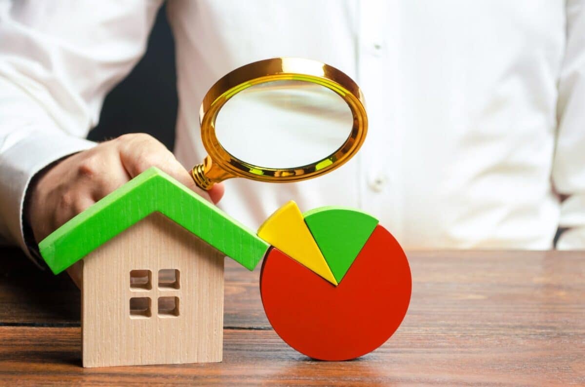 A man studies a pie chart with a magnifying glass near the house figure.