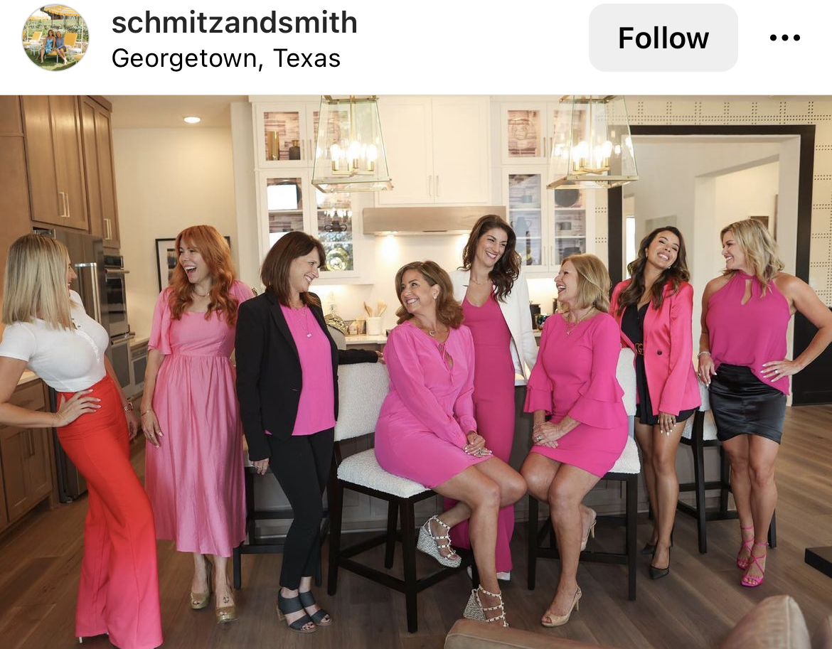 A group of women posing for a picture, all wearing pink and black business attire.