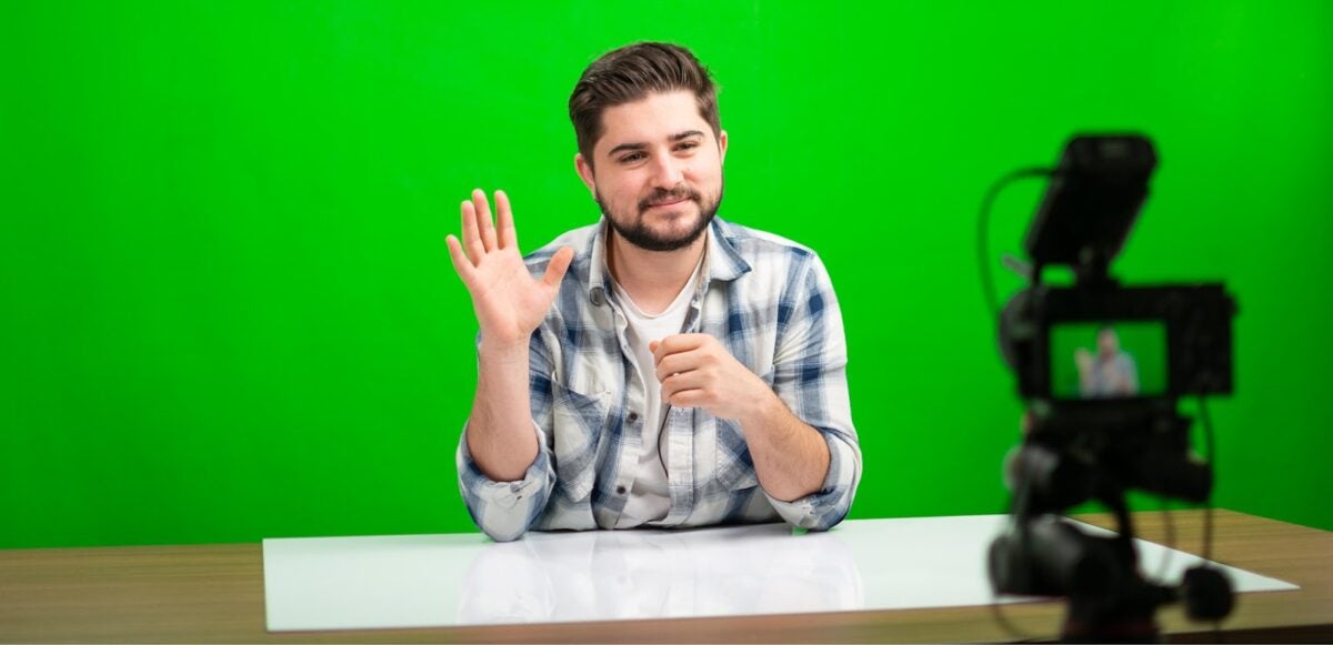 Man in front of a green screen waving at a camera.