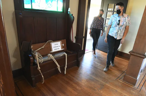 Two people walking through a door looking at a skeleton decoration on a entryway bench.