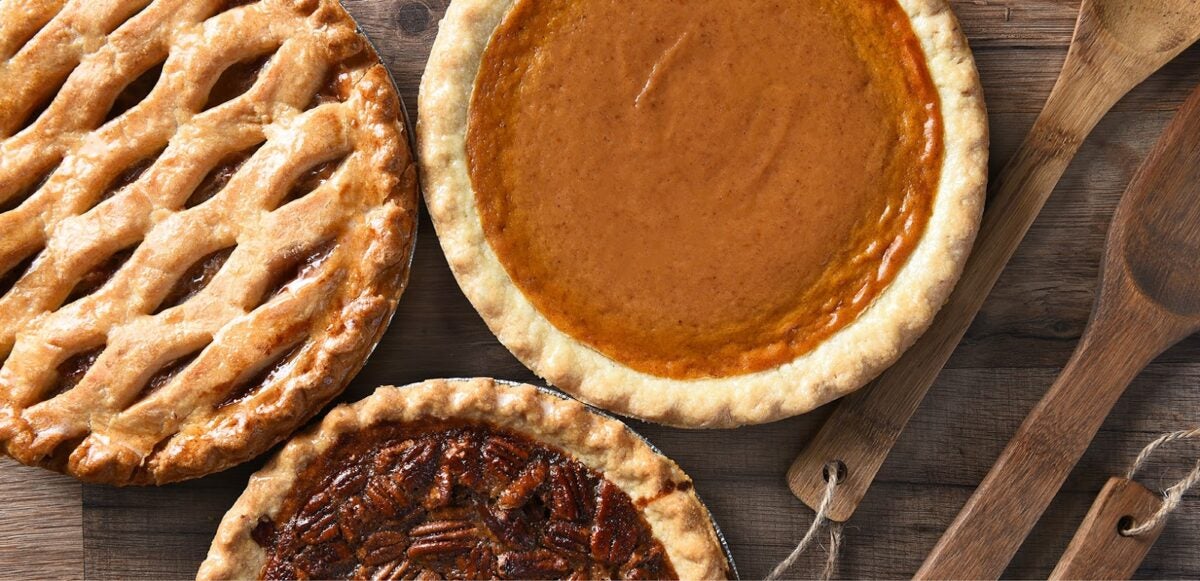 Thanksgiving apple, pumpkin, and pecan pies with wooden serving utensils.