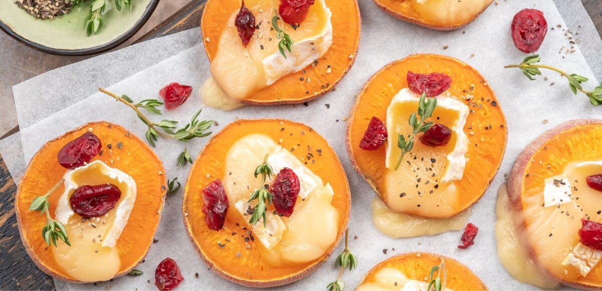 Sweet potatoes appetizers arranged on wax paper with melting brie, cranberry, and rosemary sprigs.