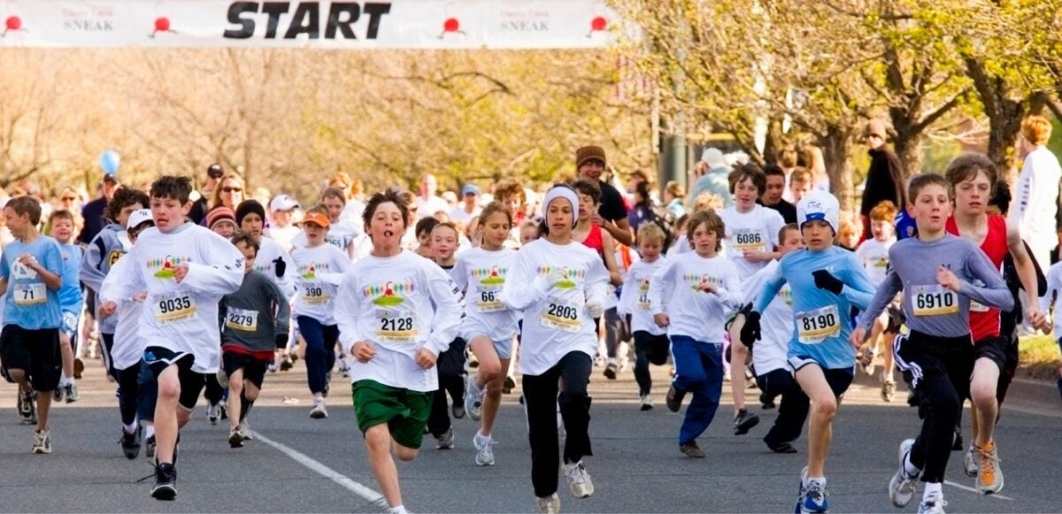 A large group of kids running in a street race.