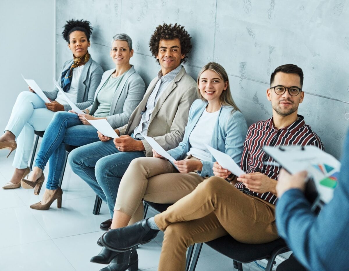 People sitting in chairs holding resumes waiting to be called for an interview.