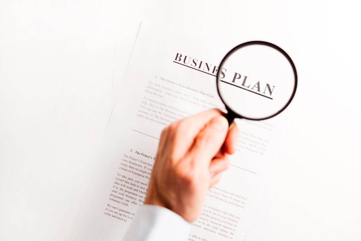 A hand holding a magnifying glass about the title of a business plan.