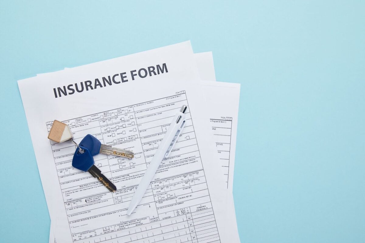 Top view of insurance form, key and pen on blue background.