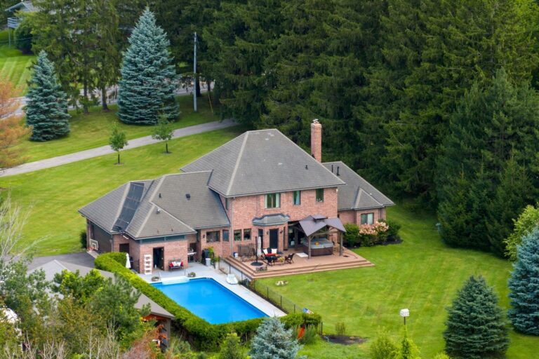 Aerial view of a large brick house with a backyard pool and spacious lawn, captured using drone photography for real estate marketing.