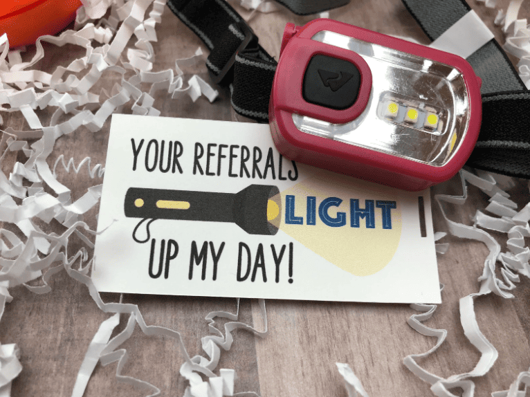 Flashlight gift with tag saying, "Your referrals light up my day!" with shredded paper decor.