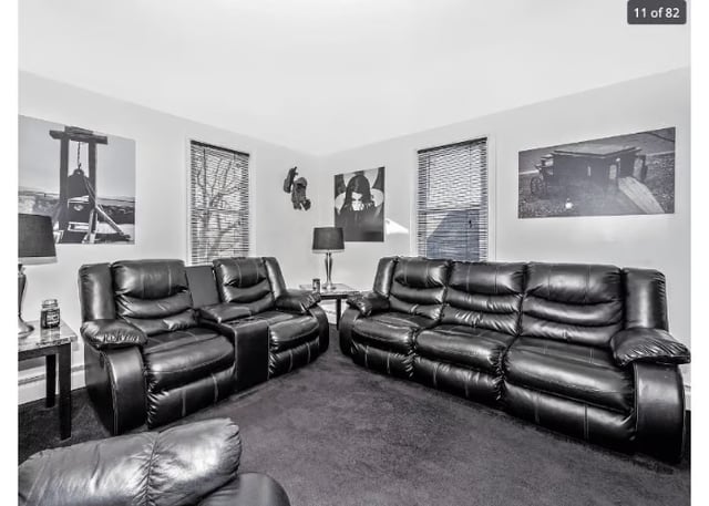 A living room with gray walls and darker gray carpet. There are two leather sofas and black-and-white art on the wall.