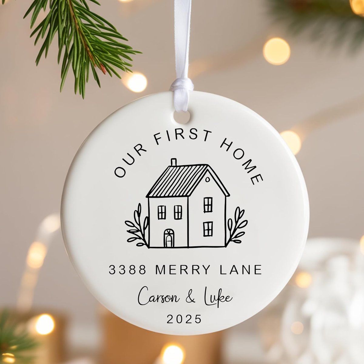 Christmas ornament that says "Our First Home". The ornament is white with a cartoon image of a home and gives an address, the name of the couple, and the year.