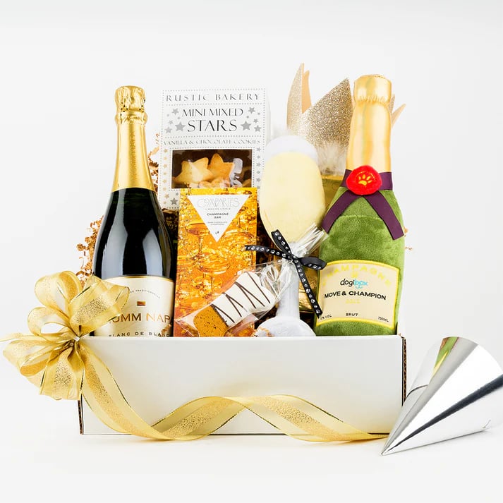 A gift basket for both a human and dog filled with items included a bottle of champagne and a plush champagne bottle for a dog.