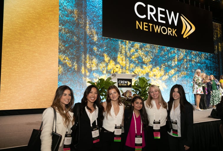 A group of women posing together in front of the CREW Network stage.