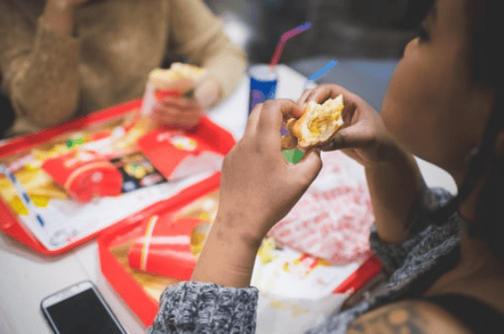Young woman eating sandwich with friends in fast food restaurant